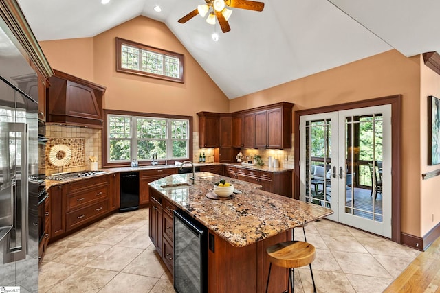 kitchen with a healthy amount of sunlight, light stone counters, wine cooler, decorative backsplash, and a center island with sink