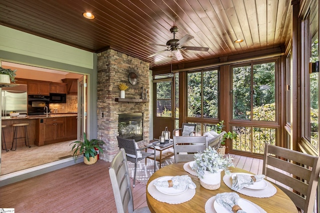 sunroom / solarium with ceiling fan, wooden ceiling, and a fireplace