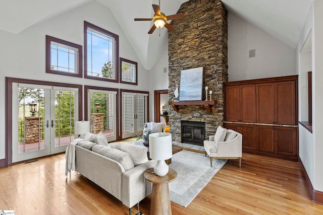 living room featuring high vaulted ceiling, a fireplace, light hardwood / wood-style floors, and ceiling fan