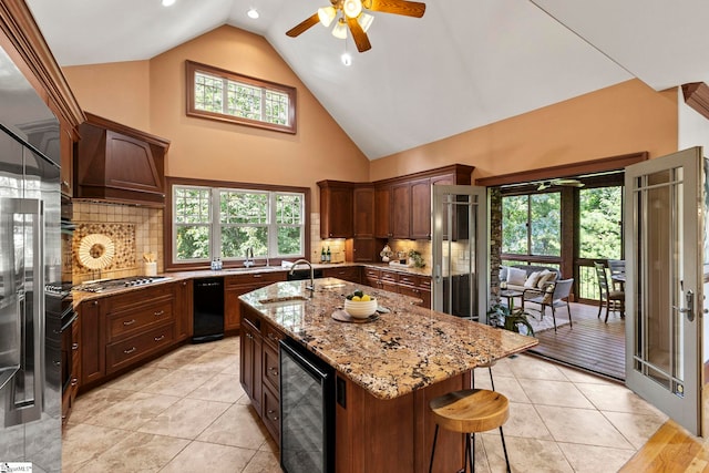 kitchen featuring backsplash, wine cooler, light stone counters, and a kitchen island with sink