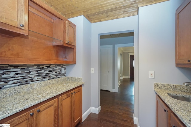 kitchen featuring wood ceiling, backsplash, sink, light stone countertops, and dark wood-type flooring