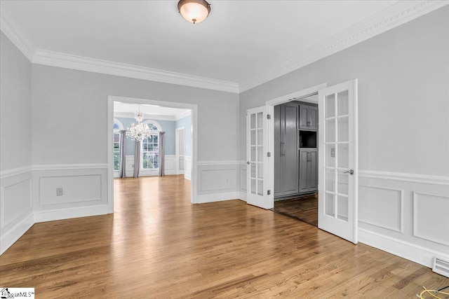 spare room with hardwood / wood-style flooring, an inviting chandelier, crown molding, and french doors