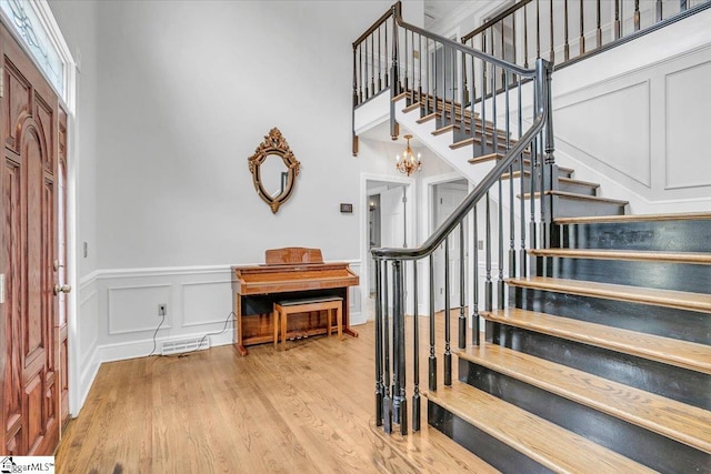 foyer with light hardwood / wood-style floors, an inviting chandelier, and a towering ceiling