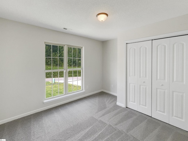 unfurnished bedroom featuring carpet, visible vents, baseboards, a closet, and a textured ceiling