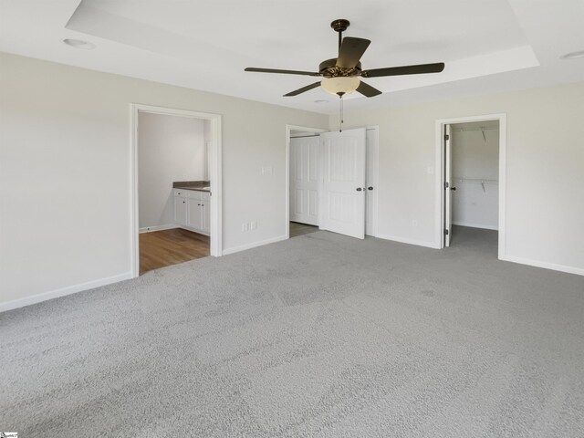 unfurnished bedroom featuring ensuite bathroom, carpet flooring, a walk in closet, a closet, and ceiling fan