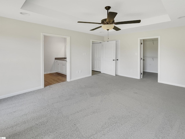 unfurnished bedroom featuring a raised ceiling, connected bathroom, carpet floors, baseboards, and ceiling fan