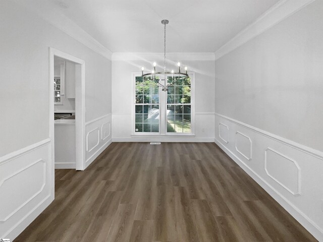 unfurnished dining area with dark hardwood / wood-style floors, an inviting chandelier, and crown molding