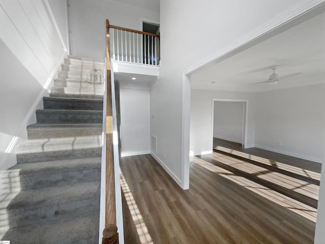 stairs with a towering ceiling, baseboards, wood finished floors, and a ceiling fan