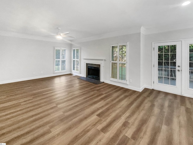 unfurnished living room featuring baseboards, wood finished floors, a healthy amount of sunlight, and a fireplace with raised hearth