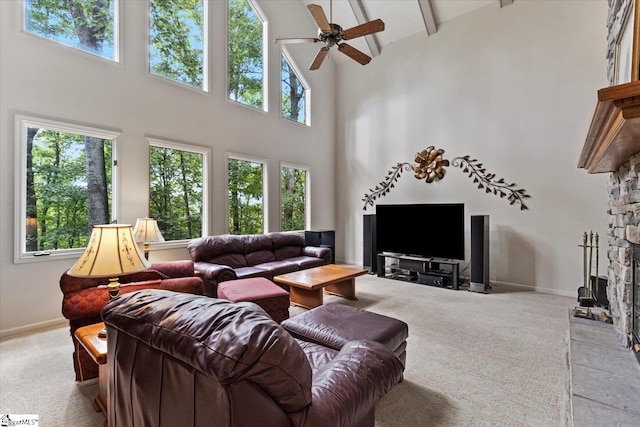 carpeted living room featuring a healthy amount of sunlight, ceiling fan, a stone fireplace, and high vaulted ceiling