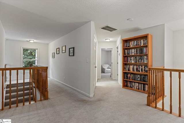 corridor with a textured ceiling and light colored carpet