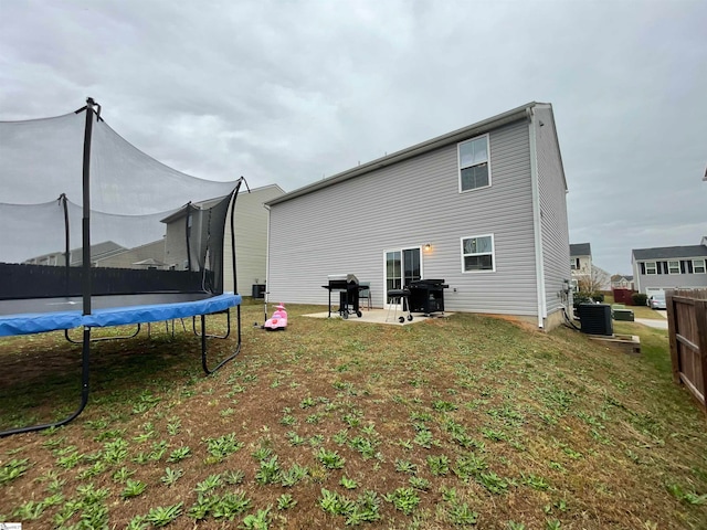 back of house featuring central AC unit, a patio area, a lawn, and a trampoline