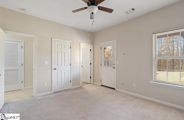 unfurnished bedroom with light carpet, multiple closets, and ceiling fan