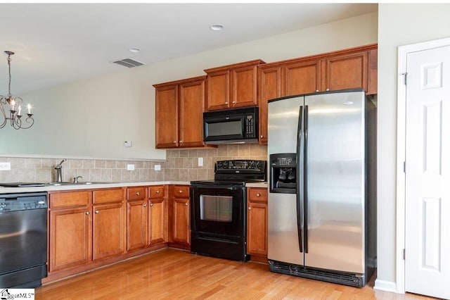 kitchen featuring light wood-type flooring, pendant lighting, backsplash, black appliances, and an inviting chandelier