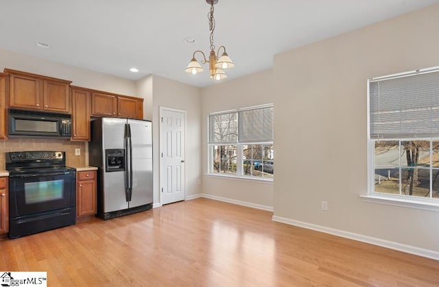 kitchen with light hardwood / wood-style floors, a notable chandelier, black appliances, pendant lighting, and tasteful backsplash