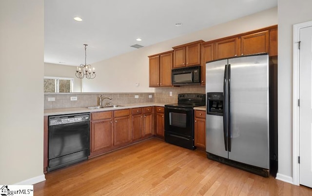 kitchen with black appliances, light hardwood / wood-style flooring, hanging light fixtures, sink, and a chandelier