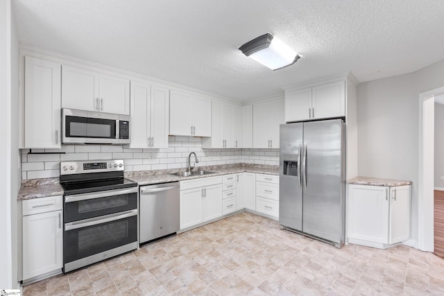 kitchen featuring backsplash, white cabinets, sink, a textured ceiling, and appliances with stainless steel finishes