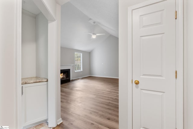 unfurnished living room with ceiling fan, lofted ceiling, a textured ceiling, and light hardwood / wood-style flooring