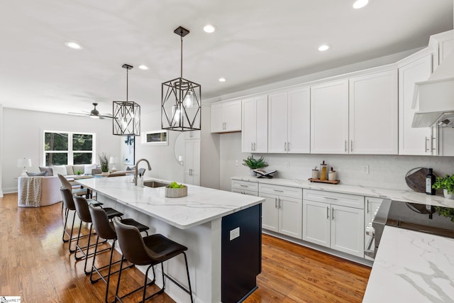 kitchen featuring hardwood / wood-style floors, white cabinetry, sink, ceiling fan, and a center island with sink