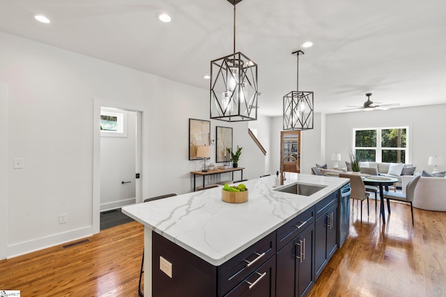 kitchen featuring light wood-type flooring, ceiling fan with notable chandelier, an island with sink, and sink