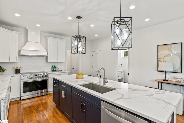 kitchen featuring a kitchen island with sink, stainless steel appliances, sink, custom range hood, and white cabinets