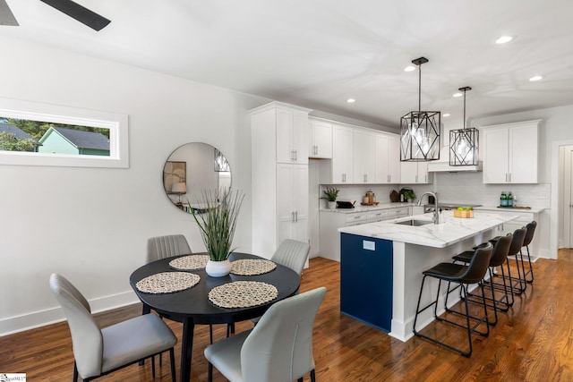 kitchen with light stone counters, white cabinetry, sink, dark wood-type flooring, and a kitchen island with sink