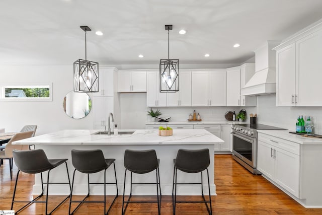 kitchen with wood-type flooring, a kitchen island with sink, sink, white cabinetry, and stainless steel range with electric cooktop