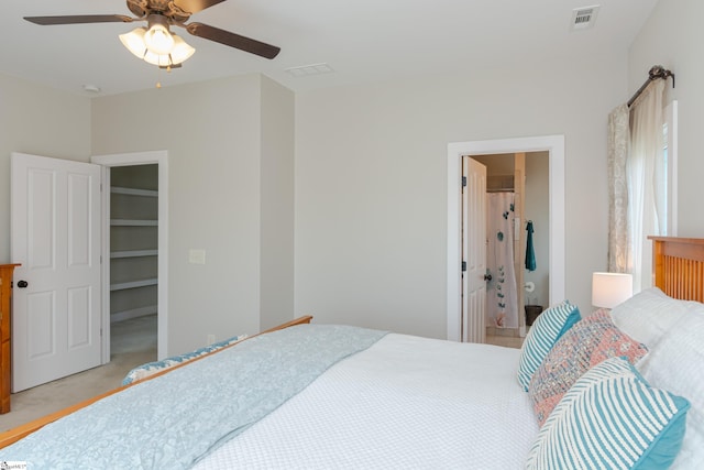 bedroom featuring ceiling fan, light colored carpet, ensuite bath, and a spacious closet