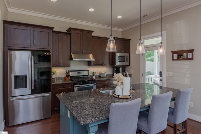 kitchen with dark wood-type flooring, dark stone counters, a center island with sink, and appliances with stainless steel finishes