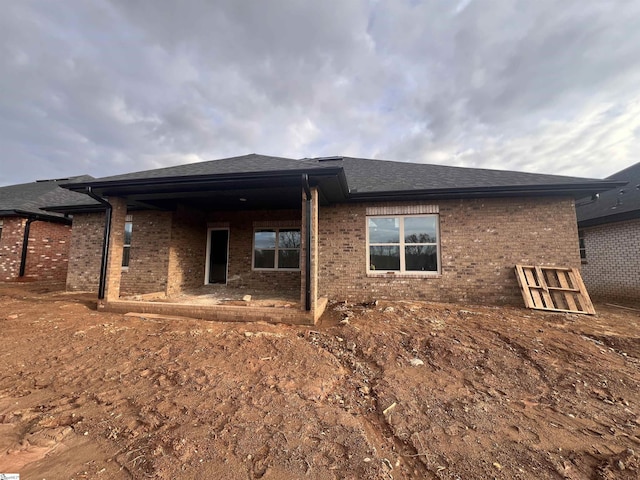 back of property with a shingled roof and brick siding