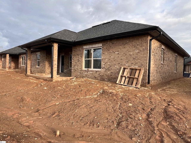 rear view of house featuring roof with shingles and brick siding