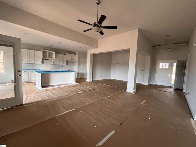 unfurnished living room featuring baseboards and ceiling fan with notable chandelier