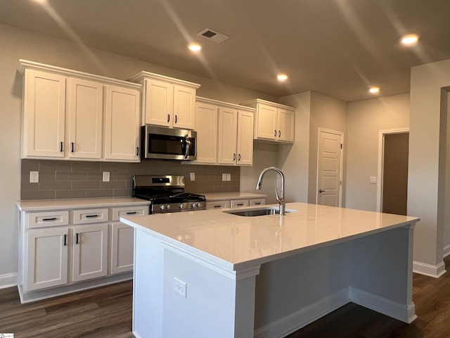 kitchen featuring tasteful backsplash, appliances with stainless steel finishes, white cabinetry, a sink, and an island with sink