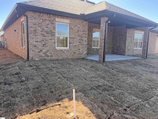 rear view of house featuring a shingled roof, cooling unit, a patio area, and brick siding