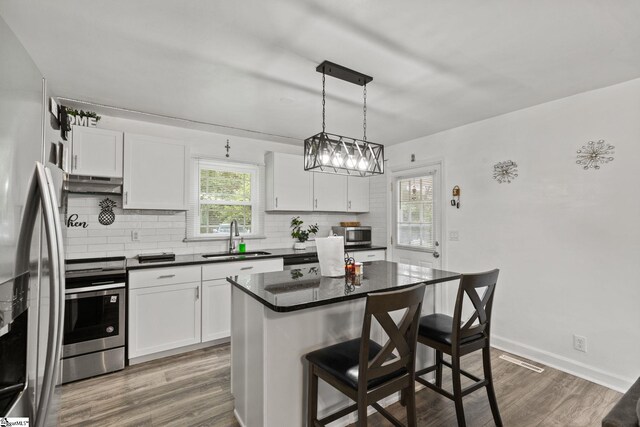 kitchen with a center island, white cabinetry, decorative light fixtures, and stainless steel appliances