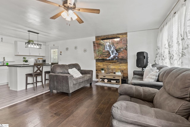 living room with dark wood-type flooring, sink, ceiling fan, and wooden walls