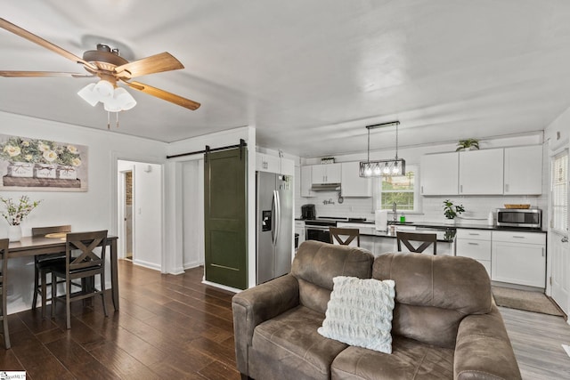 living room featuring a barn door, ceiling fan, sink, and dark hardwood / wood-style flooring