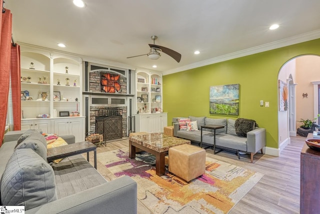 living room featuring a stone fireplace, ceiling fan, crown molding, and light hardwood / wood-style flooring