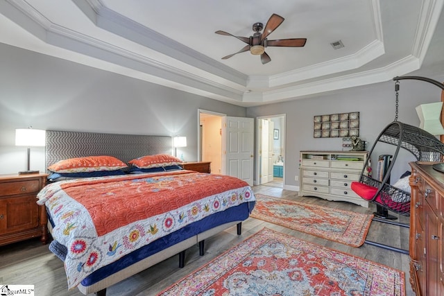 bedroom with a tray ceiling, connected bathroom, light hardwood / wood-style floors, and ceiling fan