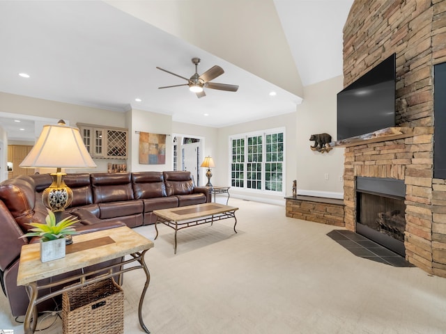 living room featuring carpet flooring, ceiling fan, vaulted ceiling, and a stone fireplace