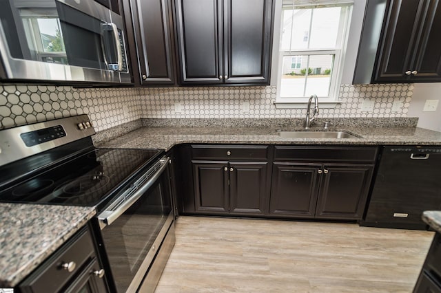 kitchen with stone counters, light wood-style flooring, appliances with stainless steel finishes, decorative backsplash, and a sink