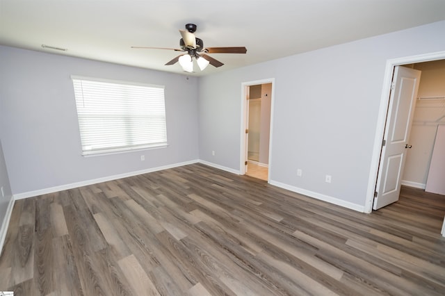 unfurnished bedroom with visible vents, a walk in closet, baseboards, wood finished floors, and a closet