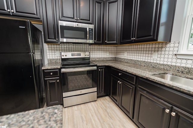kitchen featuring backsplash, stainless steel appliances, light wood-style floors, and dark cabinetry