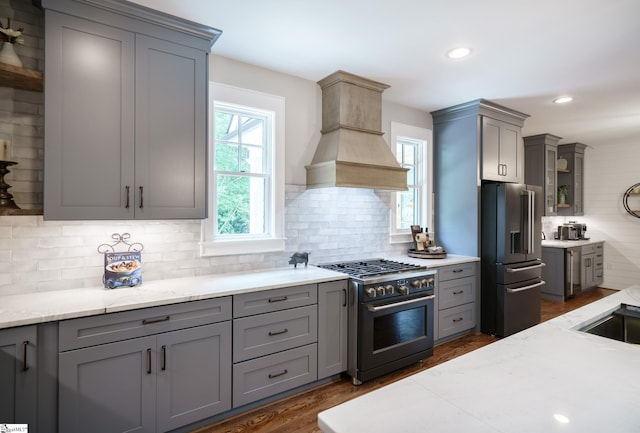 kitchen with gray cabinetry, dark hardwood / wood-style flooring, custom range hood, tasteful backsplash, and stainless steel appliances