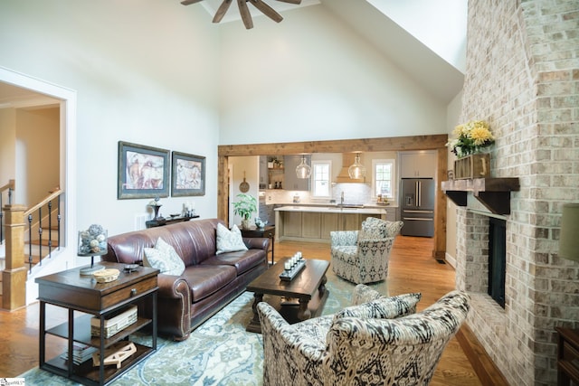 living room with hardwood / wood-style floors, sink, high vaulted ceiling, a brick fireplace, and ceiling fan