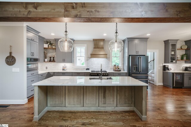 kitchen with appliances with stainless steel finishes, light stone countertops, a center island with sink, and custom exhaust hood