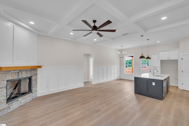 unfurnished living room featuring ceiling fan with notable chandelier, beamed ceiling, a fireplace, and light hardwood / wood-style floors