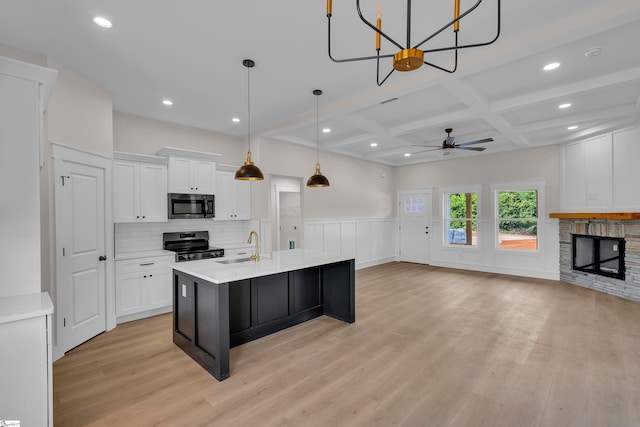 kitchen featuring a fireplace, ceiling fan with notable chandelier, coffered ceiling, black electric range oven, and a kitchen island with sink