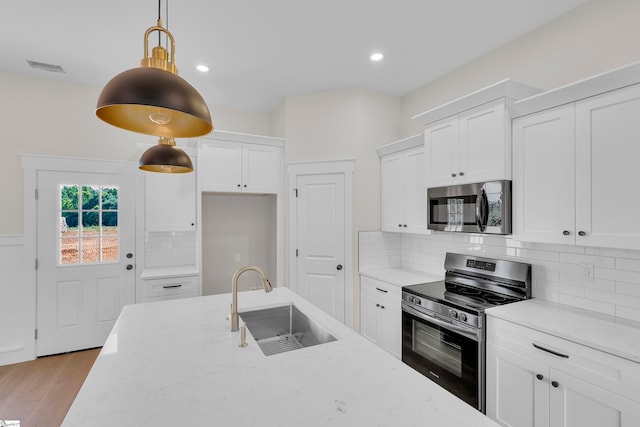 kitchen with appliances with stainless steel finishes, light hardwood / wood-style floors, hanging light fixtures, sink, and white cabinetry