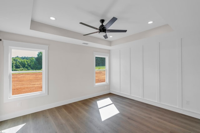 unfurnished room featuring dark wood-type flooring, a wealth of natural light, a raised ceiling, and ceiling fan